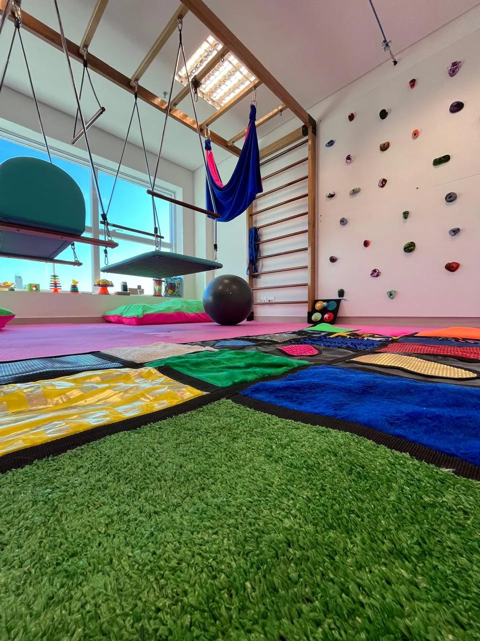 Sala de integração sensorial com balanços, tapete de texturas e parede de escalada